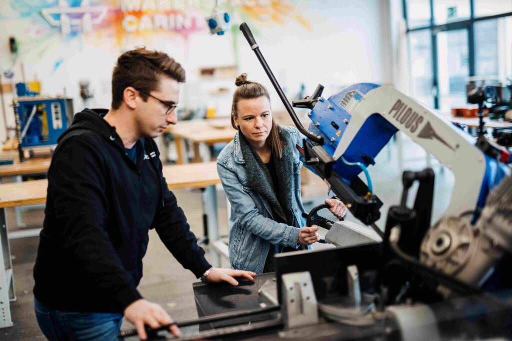 Foto aus dem Makerspace Carinthia mit zwei jungen Menschen, die an einer Maschine arbeiten 